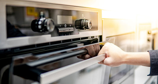 Neuer Backofen wird von einer Hand am Griff gehalten.