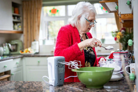 Eine Dame mit Brille steht in der Küche und bereitet etwas zu. Sie hält einen Löffel mit Mehl in der Hand.