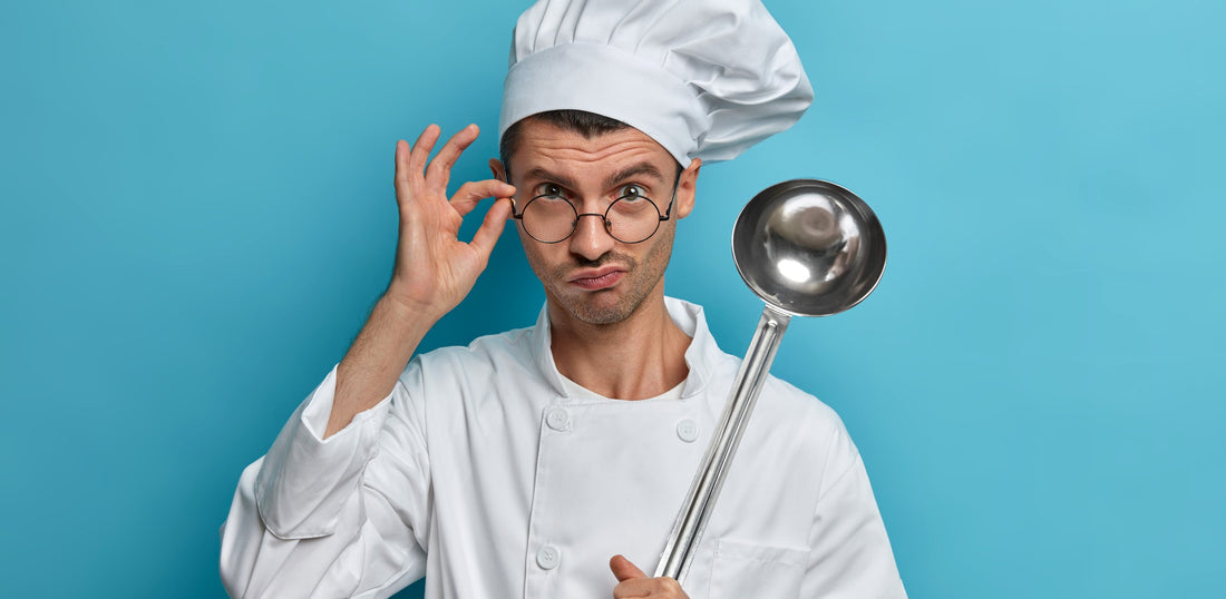 Ein Koch hält in der einen Hand eine große Suppenkelle und mit der anderen Hand seine Brille.