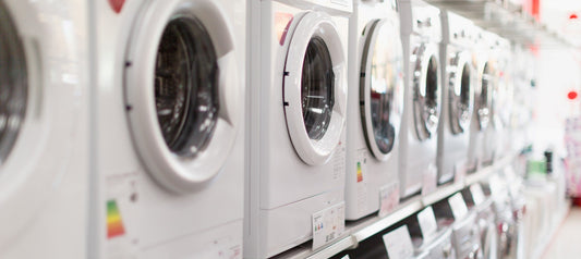 Eine große Auswahl von Waschmaschinen steht in einer langen Reihe zum Verkauf. Die Geräte sind jeweils zu zweit gestapelt.