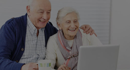 Ein älteres Paar sitzt vor einem Laptop Computer und ist fröhlich.